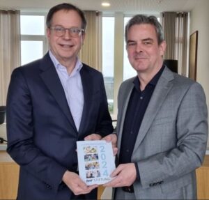 Der Vorsitzende unserer Stifterin Dr. Norbert Rollinger mit unserem Geschäftsleiter Dr. Ralph Glodek stehen zusammen und halten gemeinsam den Jahresbericht 2024 der R+V STIFTUNG in den Händen