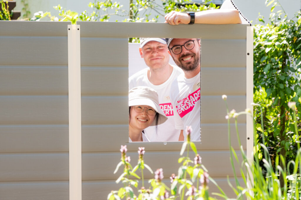 Drei R+V-Mitarbeitende schauen durch das Fenster der aufgebauten Gartenhütte