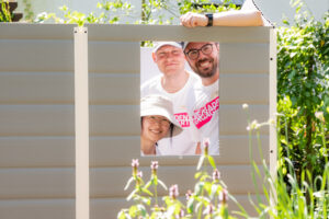 Drei R+V-Mitarbeitende schauen durch das Fenster der aufgebauten Gartenhütte